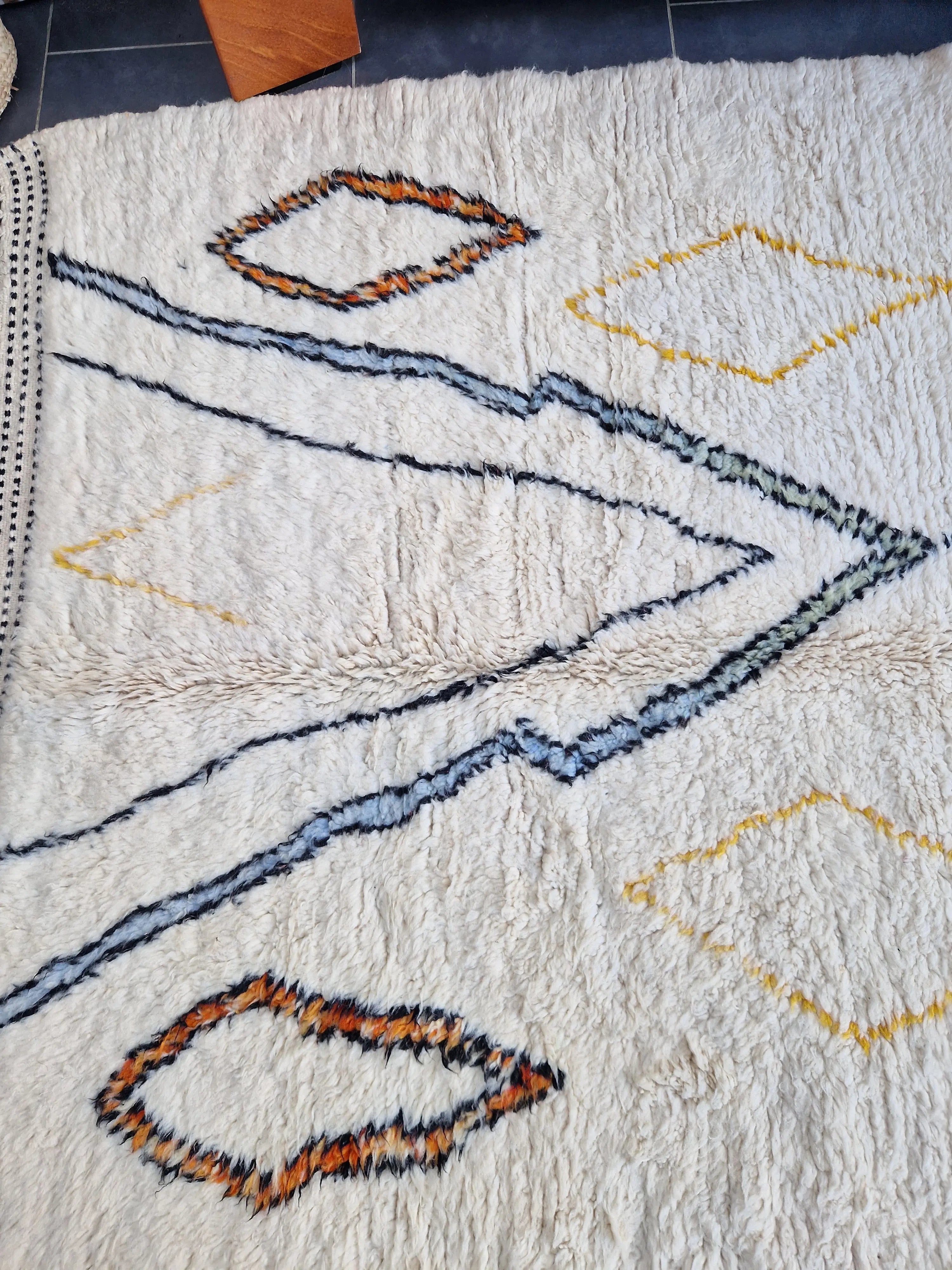 Tapis berbère beni ouarain en laine naturelle, tissé à la main au Maroc. Motifs colorés, douceur épaisse et charme artisanal. Pièce unique et chaleureuse.